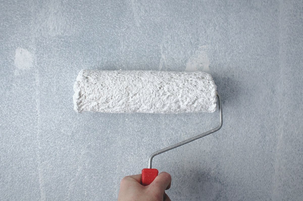 Paint roller applying white paint to an interior wall